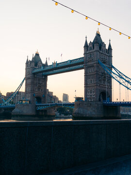 London, United Kingdom - 20 June 2025: View of the majestic Tower Bridge piercing the pastel dawn sky, its intricate stonework a testament to time, reflected in the serene waters below.