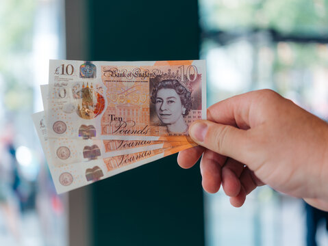London, United Kingdom - 20 June 2025: View of a hand holding new ten pound notes, the crisp paper reflecting the light, a portrait of Queen Elizabeth II gazing out from the currency.
