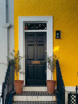 London, United Kingdom - 21 June 2025: View of a striking black door contrasts against the vibrant yellow facade, flanked by potted plants and a white brick wall.