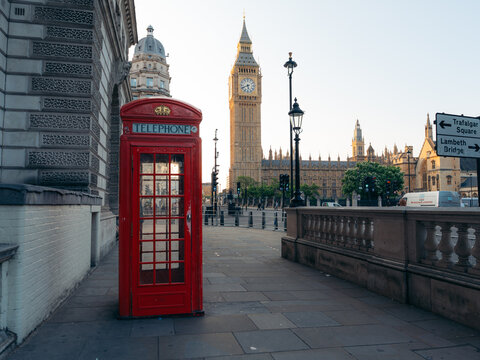 London, United Kingdom - 19 June 2025: View of a vibrant red telephone booth stands in stark contrast to the muted tones of Big Ben and the Houses of Parliament in the distance.