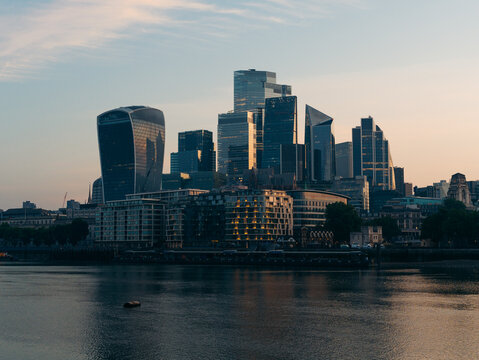 London, United Kingdom - 20 June 2025: View of the City of London's skyline, a symphony of glass and steel reflecting the muted gold of the setting sun over the tranquil Thames.