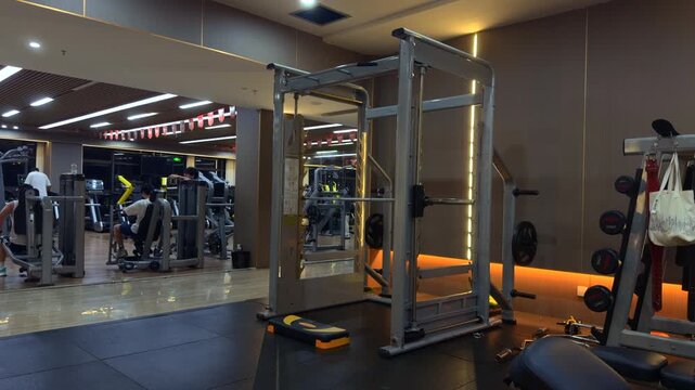 Interior view of a modern professional gym with strength training equipment.A well-equipped fitness center featuring a Smith machine, weight plates, and various workout stations. The scene shows a cle