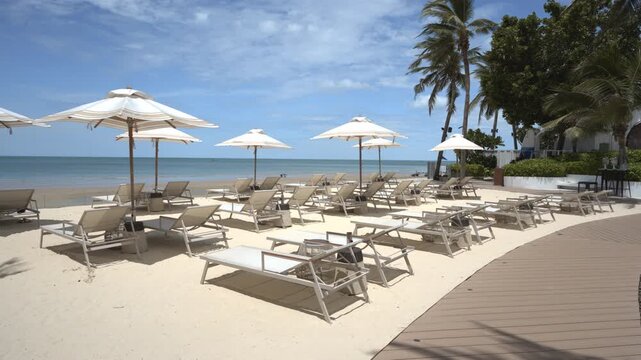 Tropical beachfront with sun loungers, white parasol on the beach shore under blue sky in summer during vacation