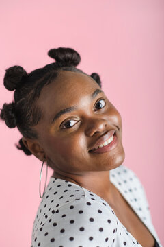 Smiling young adult woman with bantu knots against pink background