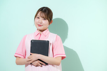 グリーン背景で介護士や保育士として働く女性の訪問介護とやりがいある仕事のイメージ　転職などのイメージにカメラ目線の笑顔　タブレットを持つ © kapinon