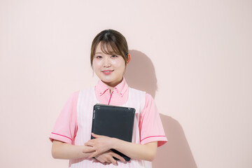 Fototapeta premium ピンク背景で介護士や保育士として働く女性の訪問介護とやりがいある仕事のイメージ 転職などのイメージにカメラ目線の笑顔 タブレットを持つ