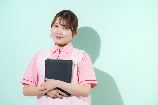 グリーン背景で介護士や保育士として働く女性の訪問介護とやりがいある仕事のイメージ　転職などのイメージにカメラ目線の笑顔　タブレットを持つ