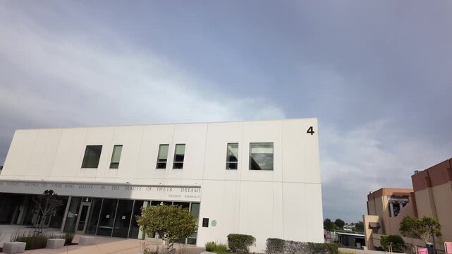 Wide-angle walking shot showing the minimalist white facade of a modern building on the Skyline College campus, located in San Bruno, California, under an overcast sky on a cloudy day