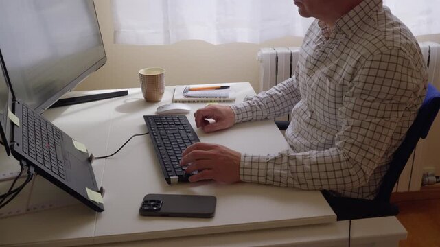 un hombre irreconocible usando el teclado del ordenador y teletrabajando desde su casa