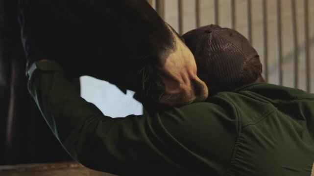 Loving bond between a man and his horse shown through a tender hug inside a stable at night