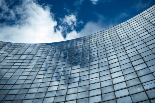 Glass facade curve in modern building reflects sky while grid lines pull perspective giving architecture a refined abstract geometric feeling
