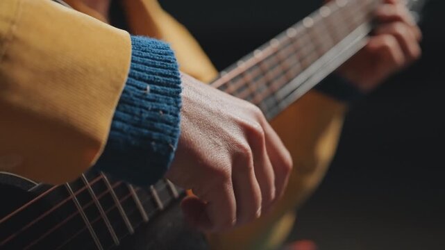 Closeup hands picking guitar strings in camping practice, focused technique shots of righthand fingerstyle and precise rhythm, camper rehearsing chord transitions with yellow jacket and blue cuff, low