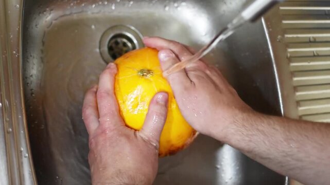 Washing melons in close-up under the tap of running water in the sink