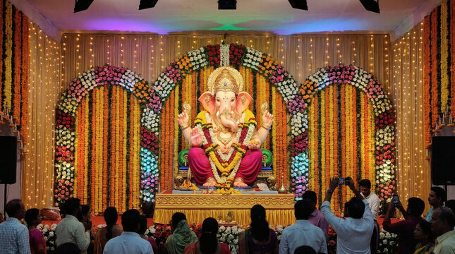 Lord Ganesha seated on decorated stage with floral arches symbolizing devotion and celebration in Hindu culture with festive background wallpaper