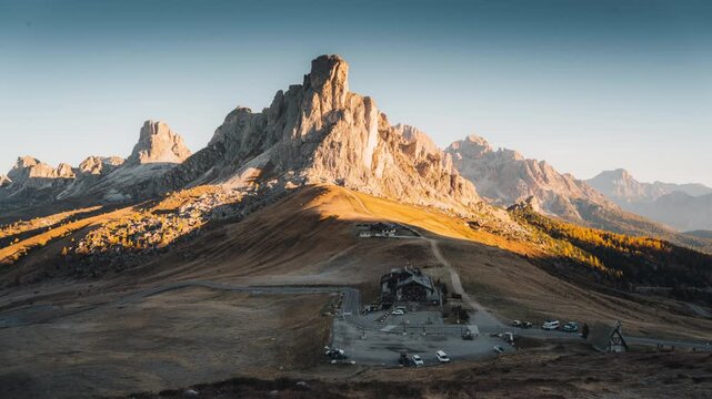 Golden sunrise over Passo Giau with Ra Gusela mountain peak, wooden lodge and winding road in Dolomites, Italy
