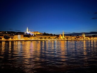 Fototapeta premium Illuminated waterfront city skyline reflected in water at blue hour
