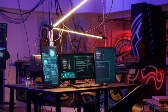Computers with malicious ransomware running code on screens in abandoned warehouse. Encryption software multiple windows and password hacking activity on monitors in dark room