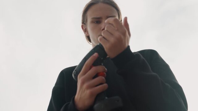 Young white man adjusting drill bit, carpenter demonstrating setup for fastener installation, handyman testing torque, creator filming tutorial under cloudy sky, hands tightening chuck, power
