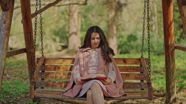 Woman reading book on wooden swing in nature