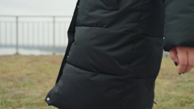 Coat sleeve and hand swinging, commuter artist improvises arm choreography, puffer texture and stitched seams, grassy embankment by metal railing, slow casual stride in muted winter light