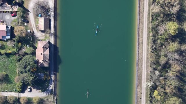 Aerial view of rowboats on the canal's tranquil green waters, contrasting sharply with the earthy tones of the adjacent pathways, Sausheim, Grand Est, France.