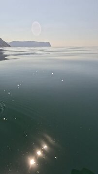 Stone skipping, calm water, serene lake surface as an object bounces and creates ripples under a bright sky.