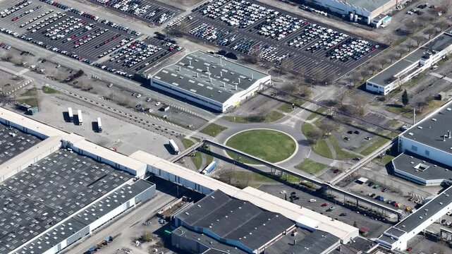 Aerial view of industrial buildings and vast parking lots filled with cars, creating a geometric pattern of light and shadow, Sausheim, Grand Est, France.