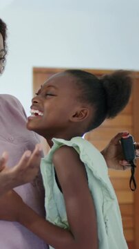 Vertical video: Approaching mother placing device on daughter in green dress by front door, hugging