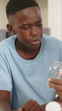Vertical video: After adult placing bulbs, teen in blue tee studying Edison bulb on kitchen counter
