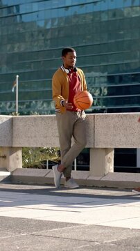 Vertical video: Receiving pass from right, man in mustard jacket cradling basketball at plaza ledge