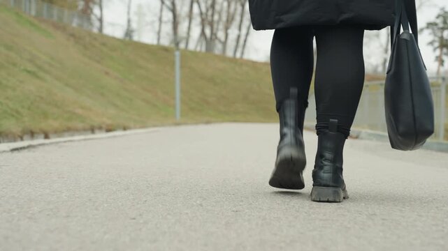 Brisk pace with winter coat moving forward. Black tote by side as boots journey along pavement. Person clad in winter coat confidently walking suburban street with bag and steady steps
