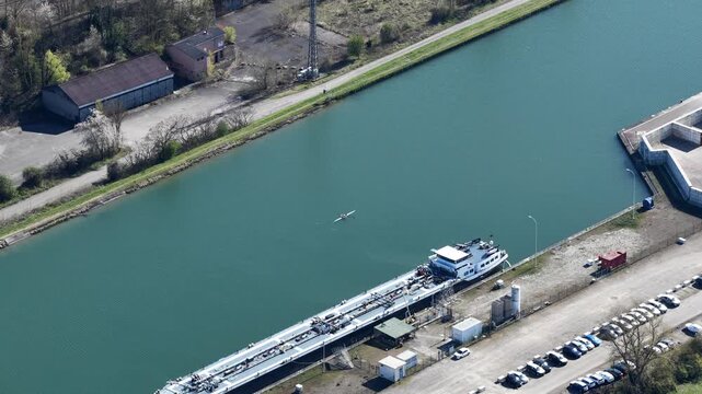 Aerial view of a canal featuring a long boat and a smaller boat with lush green trees lining the sides, Sausheim, Grand Est, France.