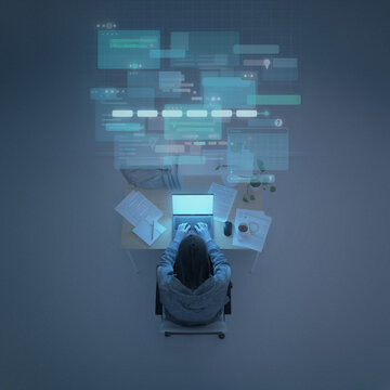 Top-Down View of Hooded Person at Cluttered Laptop Desk with Floating Digital Interface