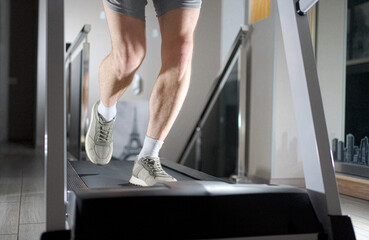 Obraz premium Close-up of Man Legs Running on Treadmill at Home. A man in sneakers and shorts running on a treadmill. Cinematic low angle shot focusing on leg muscles and movement during a cardio workout