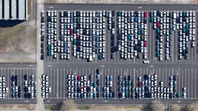 Aerial view of a vast parking lot filled with orderly rows of cars, a mosaic of whites, blacks, reds, and greens, Sausheim, Grand Est, France.
