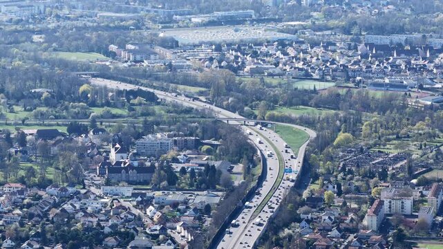 Aerial view of a busy highway cutting through the landscape, contrasting the urban sprawl with the surrounding greenery, Sausheim, Grand Est, France.
