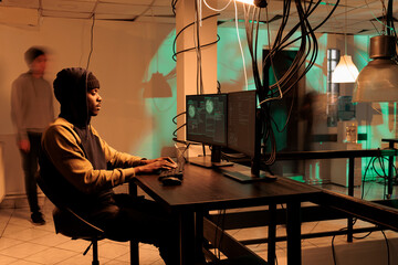 African american hacker working on spyware with encryption, causing security breach alert and accessing sensitive information for ransom. Young man hacking database server with code. © DC Studio