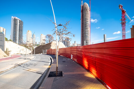 Urban street perspective in Benidorm Spain with red barrier and construction development zone as a crane rises behind modern towers