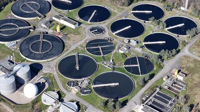 Aerial view of circular water treatment plant pools showing dark water and light colored mechanisms, creating a stark contrast, Sausheim, Grand Est, France.