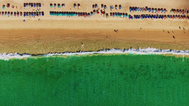 Aerial view of beach with umbrellas swimmers and waves lapping along sandy shoreline at midday, Karon on Phuket island, Thailand.
