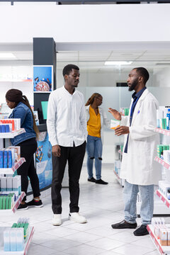 Healthcare worker recommending vitamin C supplements to a young man, assisting with medication instructions and advice at the pharmacy. Professional pharmaceutical service for wellness.