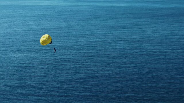 Aerial view of yellow parasail with rider gliding over open ocean in Phuket island Thailand.