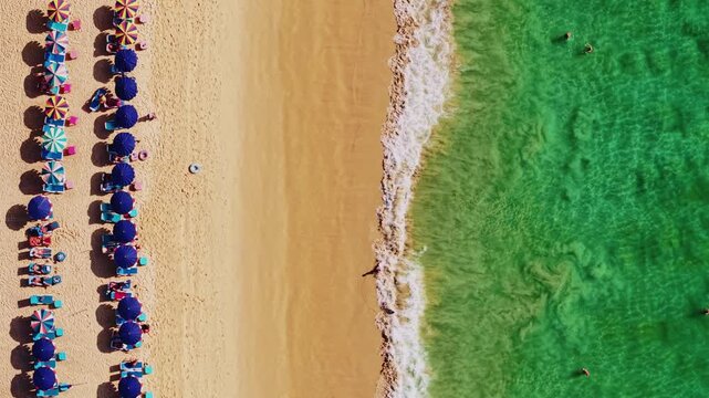 Aerial view of beach umbrellas sunbathers and swimmers along sandy shoreline, Karon on Phuket island, Thailand.