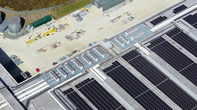 Aerial view of massive logistics distribution centre rooftop with integrated solar panel array and HVAC cooling units.