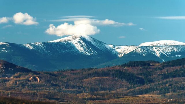 Zoom on Snezka mountain peak in Sudetes on Czech-Polish border, April, clouds, blue sky.