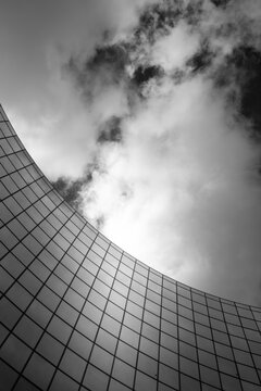 Abstract monochrome architecture skyscraper with modern curve of glass grid rising toward perspective and dramatic clouds for sleek urban design