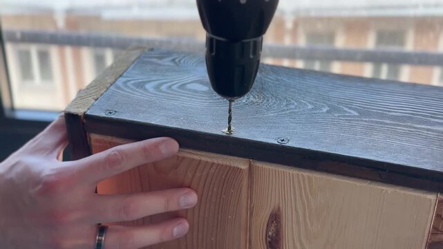 The video shows the process of drilling a hole in a wooden workpiece using an electric drill or a screwdriver.