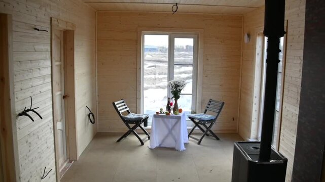 An empty room with wooden walls a window a small table two chairs fruit and a vase of flowers