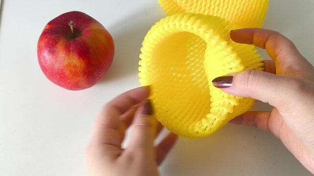 Woman packing apple in foam fruit net. Hands putting fruit in packaging for delivery
