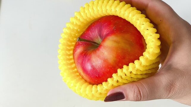 Close-up of an apple in a yellow foam net in your hand. Packaging for transportation, delivery of vegetables.